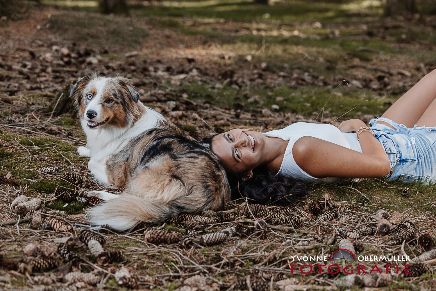 Frau liegt entspannt neben ihrem Hund im Wald