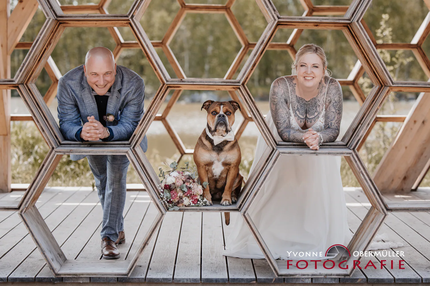 Brautpaar und Hund in einer geometrischen Holzkulisse