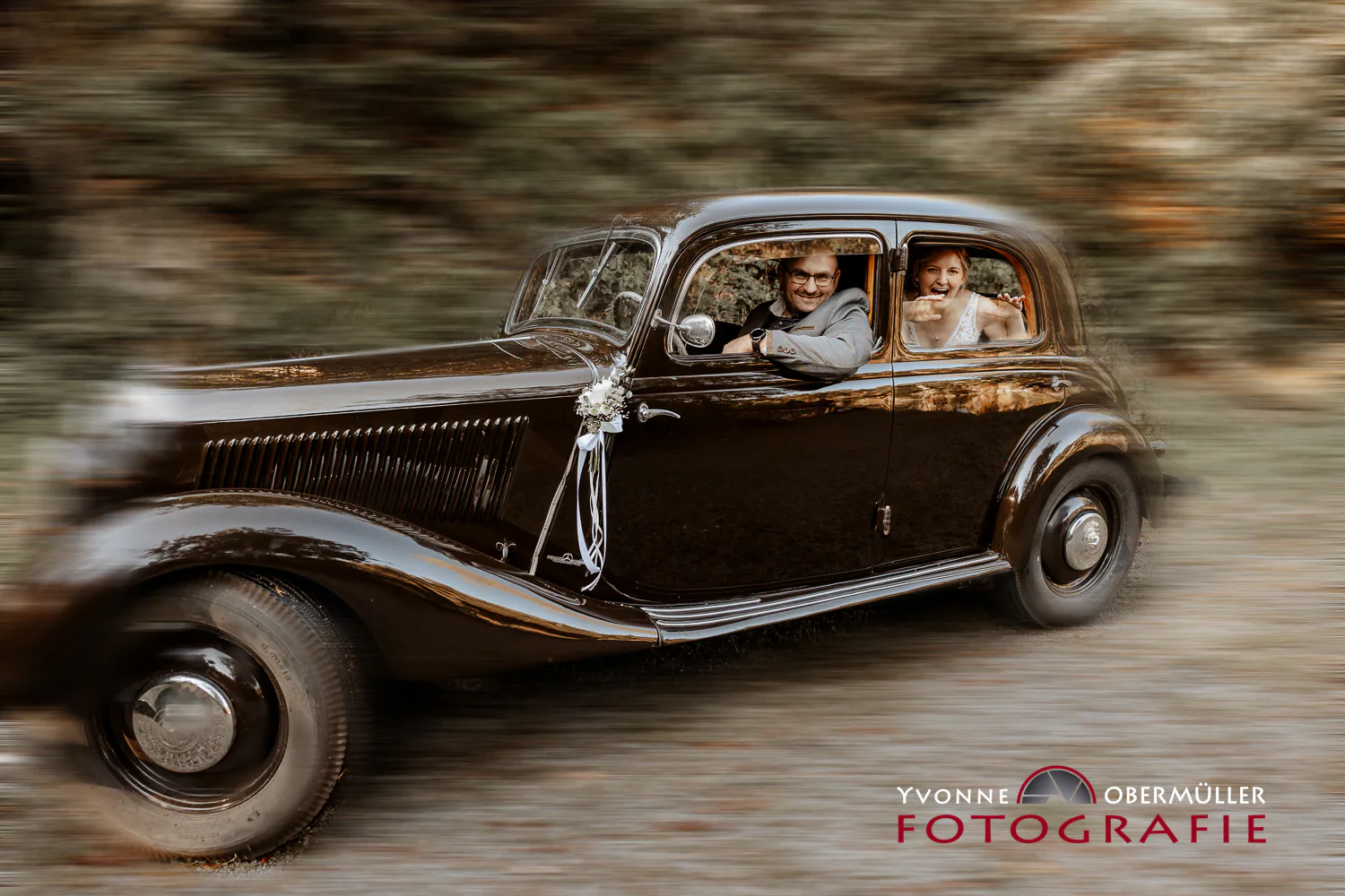 Brautpaar lacht aus einem fahrenden Oldtimer